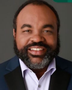 Smiling man with a dark beard and suit jacket looking at the camera. | Shawn Dandridge