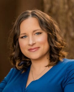 Portrait of a smiling woman with shoulder-length brown hair wearing a blue top outdoors, looking at the camera. | Lauren Draheim
